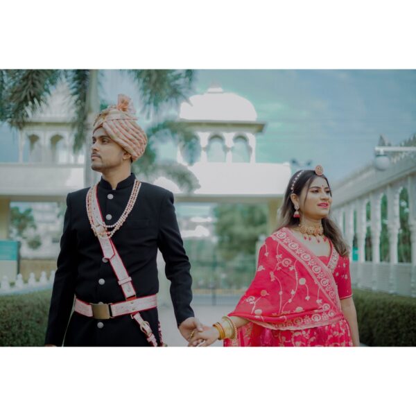 "Rajasthani couple dress in traditional attire, posing elegantly against a backdrop of intricate architectural details."