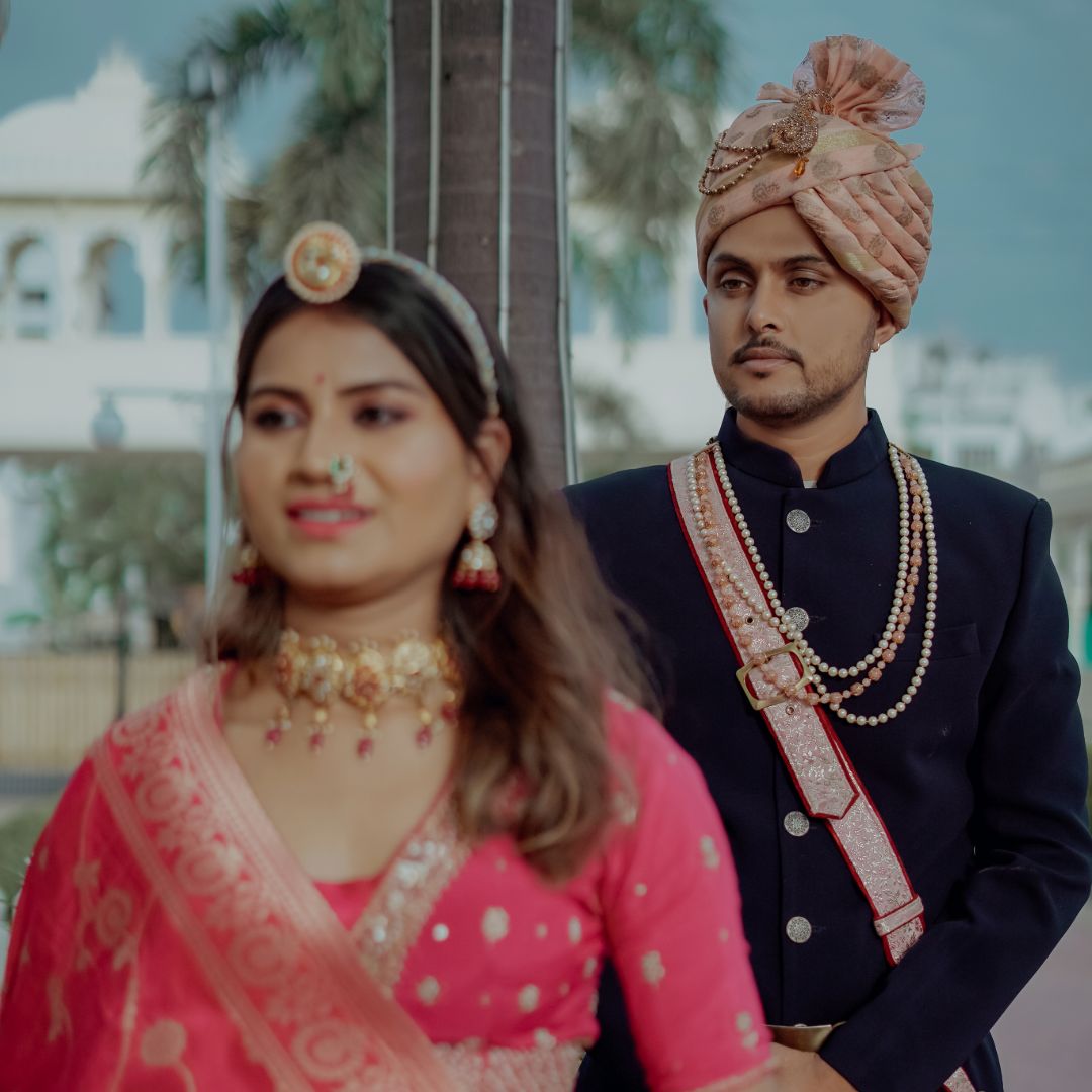 Rajasthani couple dress in traditional attire, posing elegantly against a backdrop of intricate architectural details.