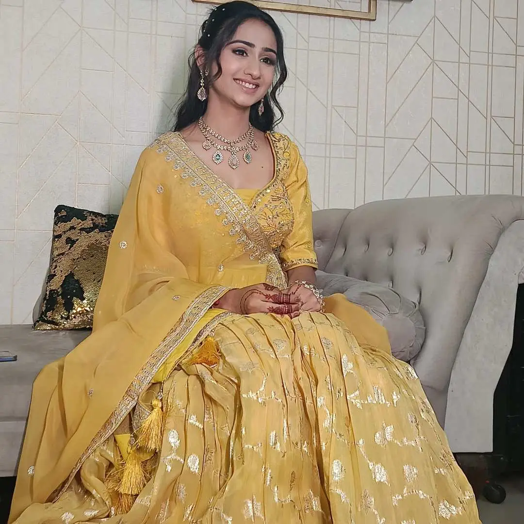 Bride wearing yellow Haldi Lehenga on Rent, seated with a smile and traditional jewellery.