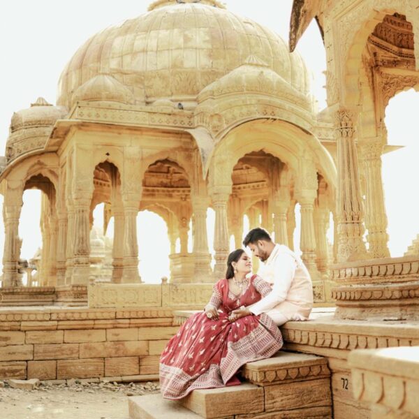 Matching couple dresses on rent in Udaipur – bride in red lehenga and groom in sherwani posing at royal venue