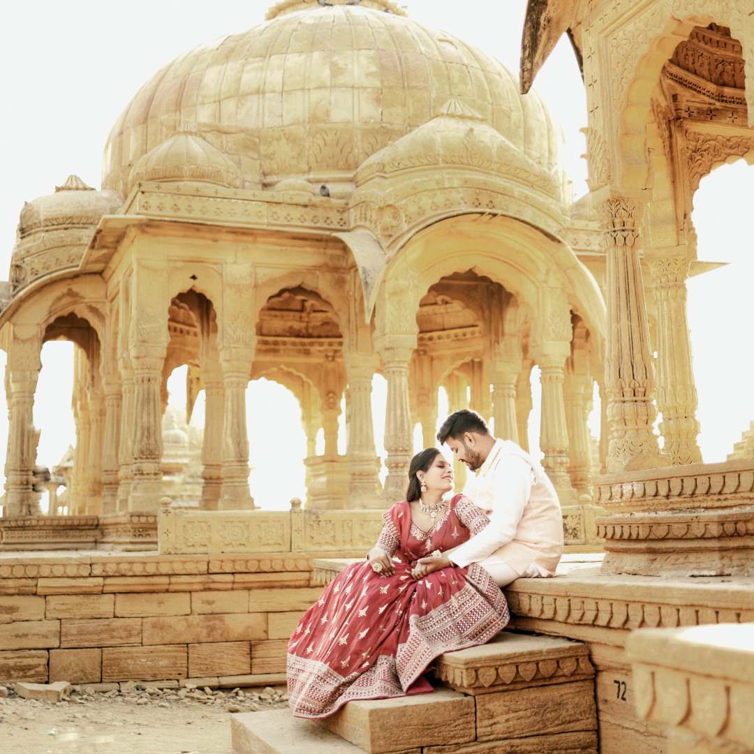 Matching couple dresses on rent in Udaipur – bride in red lehenga and groom in sherwani posing at royal venue