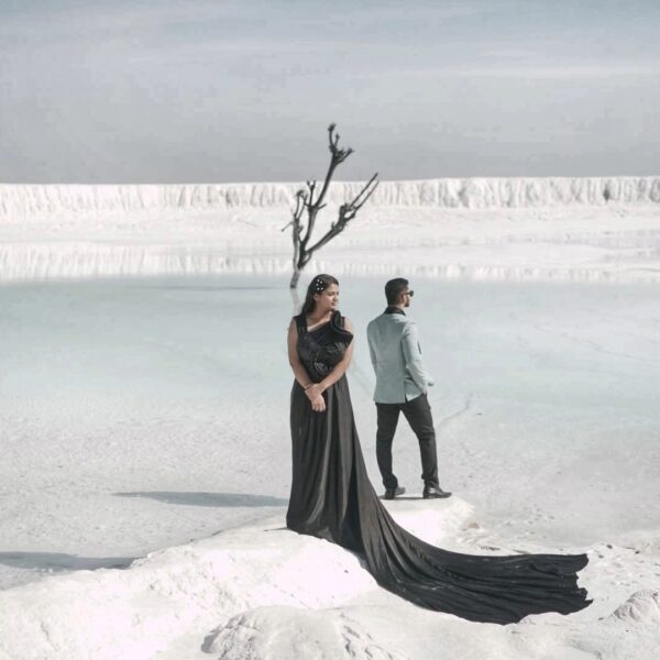 Couple wearing black trail gown and suit posing for a marble slurry photoshoot in Udaipur with stunning white backdrop.