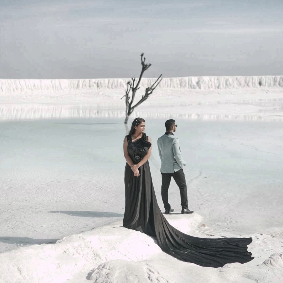 Couple wearing black trail gown and suit posing for a marble slurry photoshoot in Udaipur with stunning white backdrop.